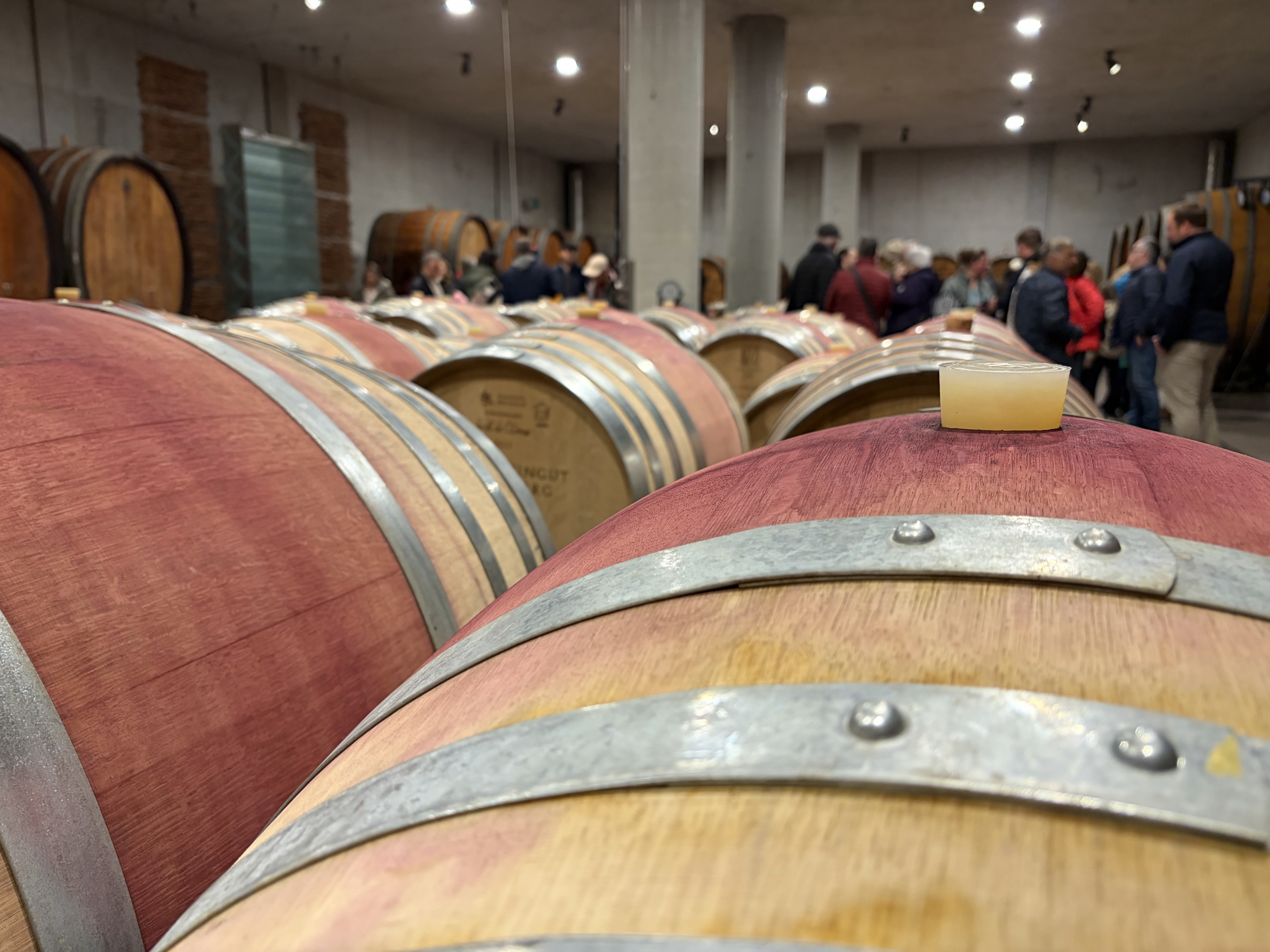 Holzfasskeller mit Weinfässern und Besuchern.