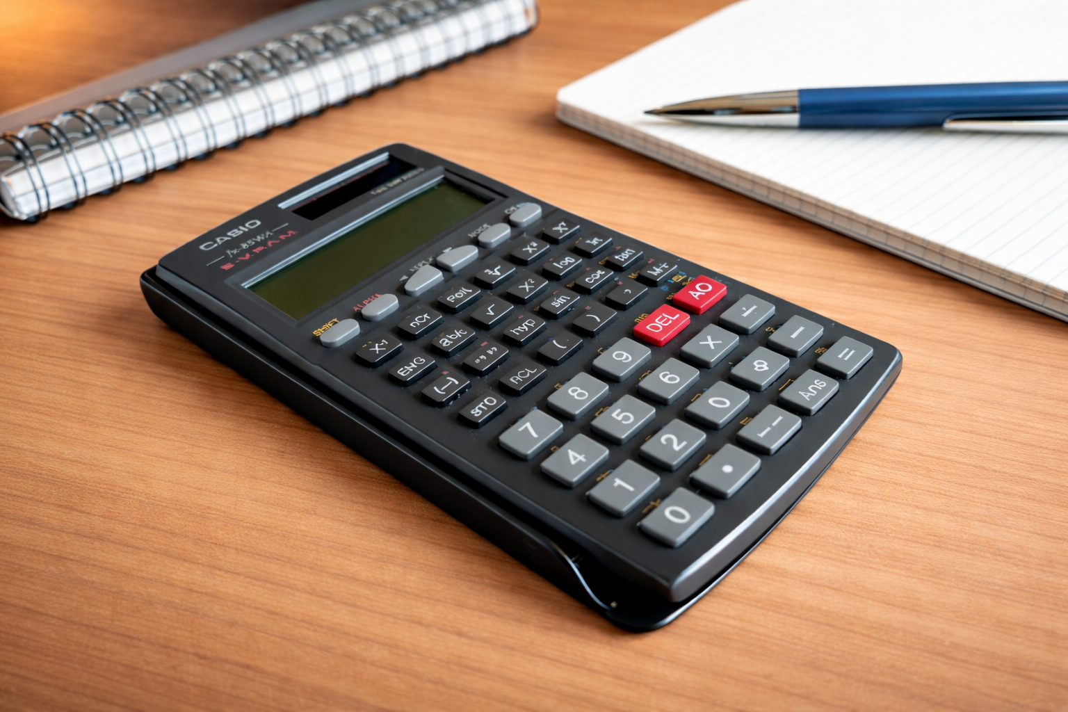 Nahaufnahme eines Taschenrechners mit Notizbuch und Stift im Hintergrund.